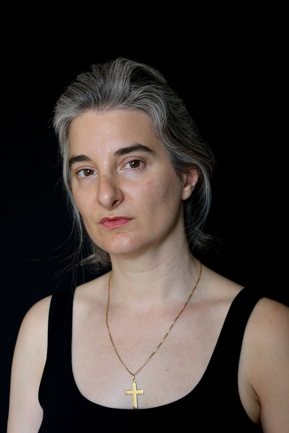 Porträt einer Schauspielerin mit silbergrauen Haaren, intensiver, nachdenklicher Blick auf schwarzem Hintergrund.