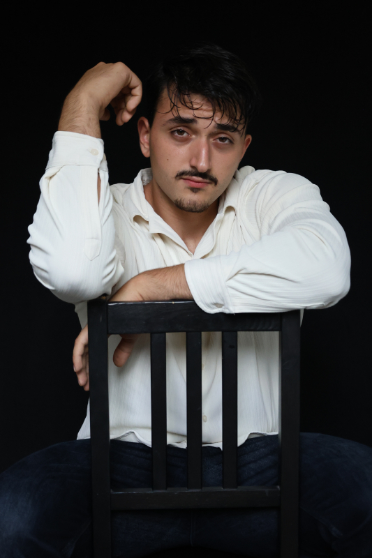 Ganzkörperfoto eines jungen Mannes, Schauspieler, schwarzer Hintergrund, skeptischer Blick, künstlerisch.