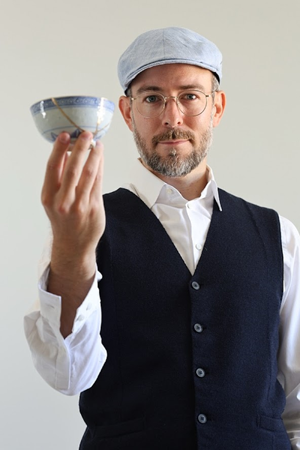 Halbkörper-Porträt eines Mannes im Fotostudio – hält eine Kintsugi-Tasse in der Hand, scharfer Blick in die Kamera.