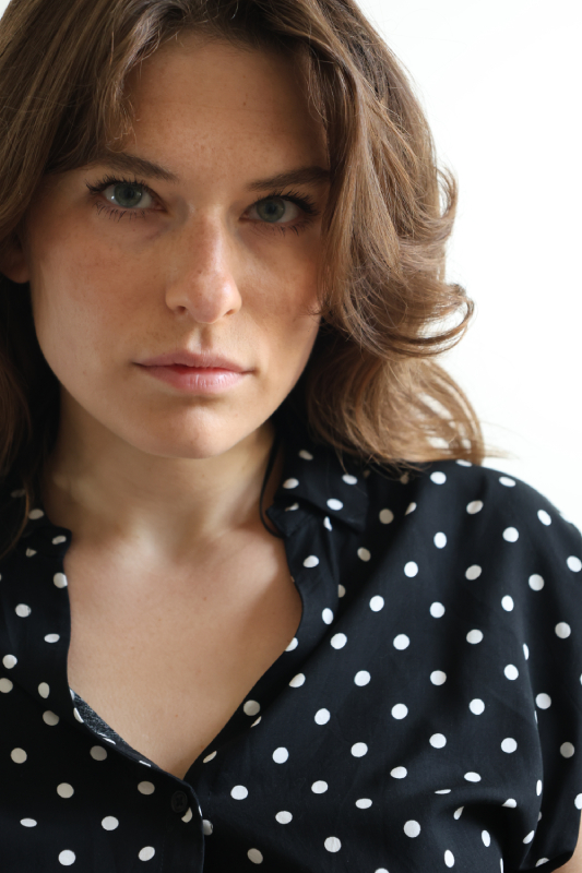 Portraitfoto einer jungen Frau, Fotomodel – tiefer Blick, schwarze Bluse mit weißen Punkten.